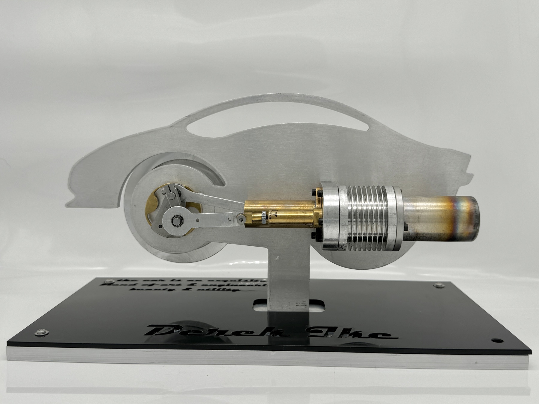 Finished Stirling engine in side profile on its laser-cut aluminum sports-car silhouette bedplate, over the engraved black acrylic base